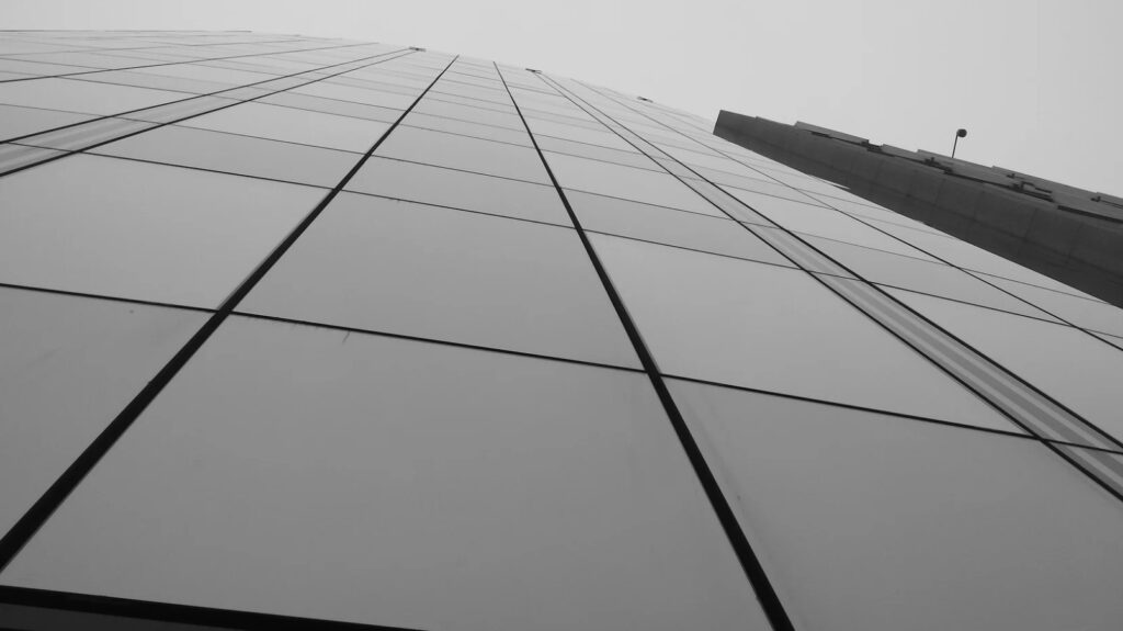 Schwarz-weiß Foto eines modernen Wolkenkratzers, der in den Himmel ragt, mit reflektierenden Glasfenstern.